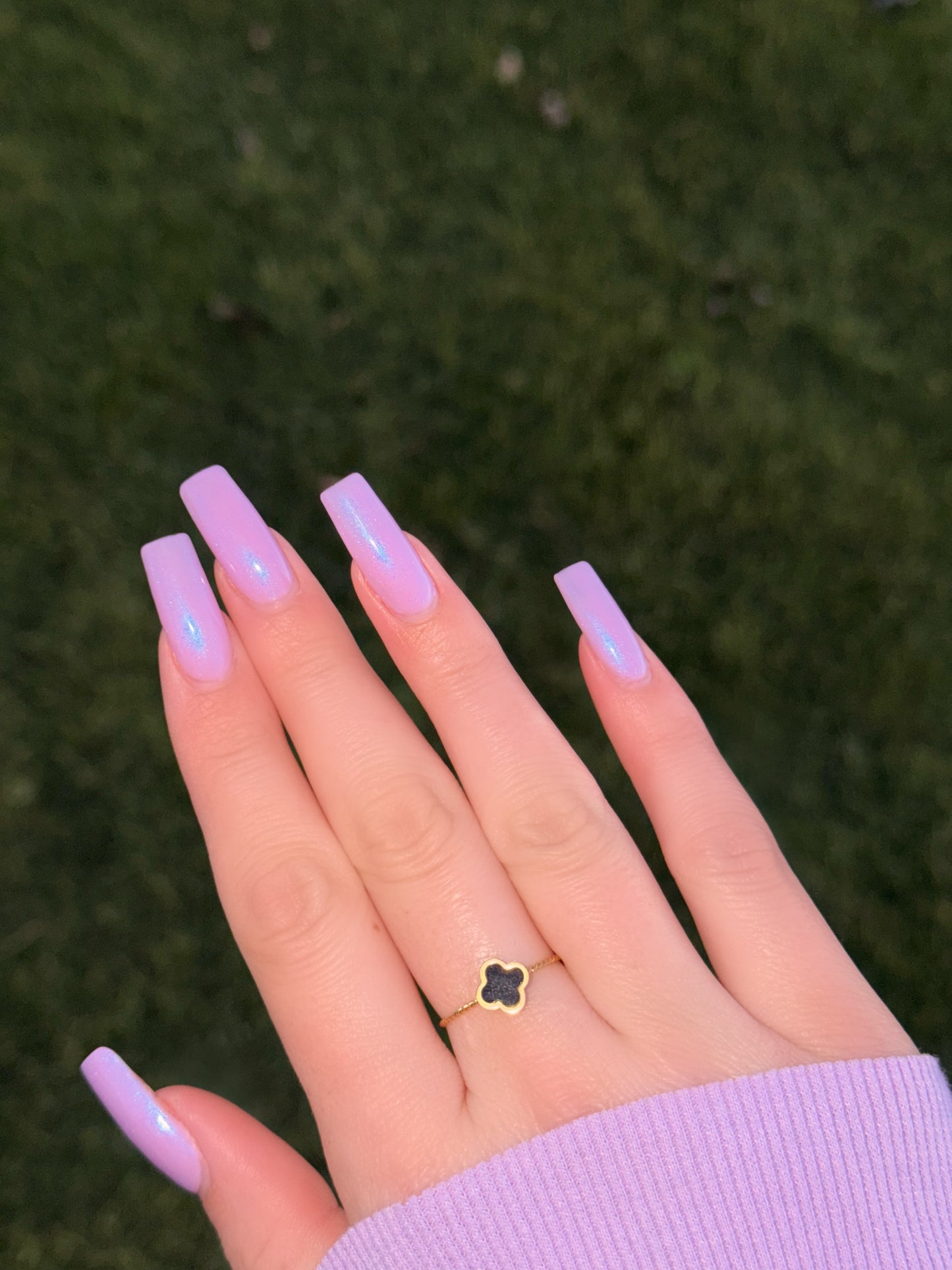 Hand with lavender nail polish and a clover-shaped ring on a blurred green background