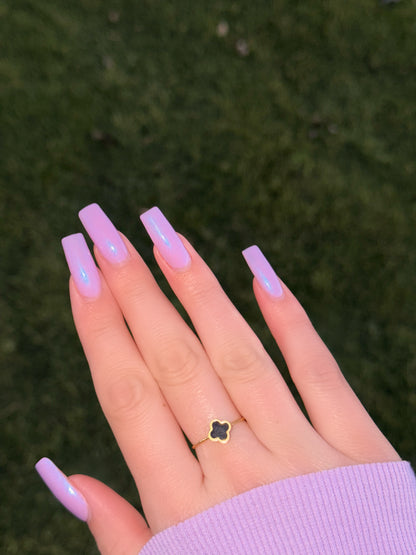 Hand with lavender nail polish and a clover-shaped ring on a blurred green background