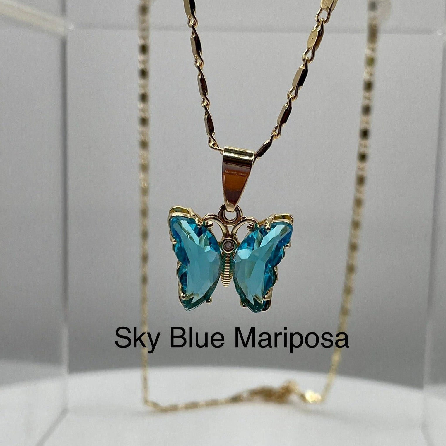 Blue butterfly pendant on gold necklace displayed on an acrylic base. Butterfly pendant. iridescent butterfly pendant. Mariposa pendant. Gold plated pendants.